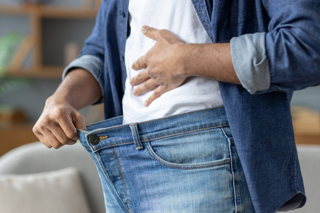 A man shows how much weight he has lost by holding out the waist of his jeans, symbolizing his successful diet.